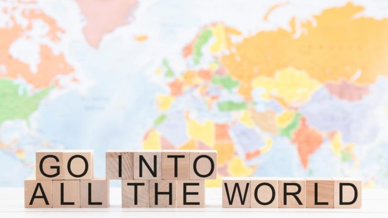 A world map with scrabble pieces that spell out "Go Into All The World" on them.